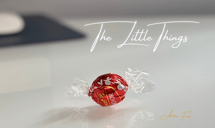 A red wrapped chocolate placed on a office desk with the words The Little Things